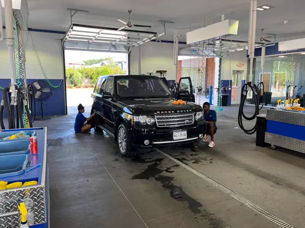 Two MEGA Auto Spa detailers working on a black Range Rover in the bright detail center