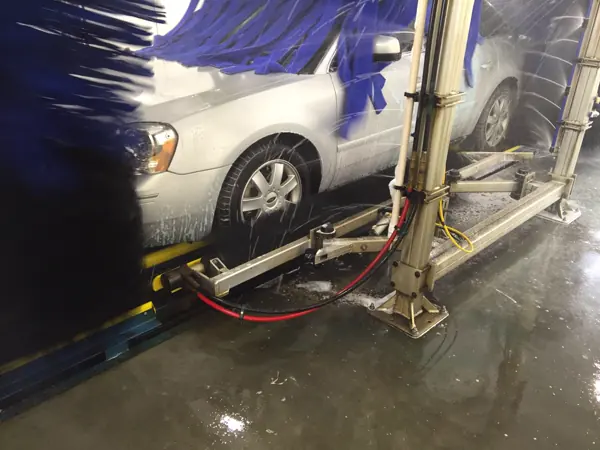 A silver car moving through the wash tunnel between blue cloth brushes