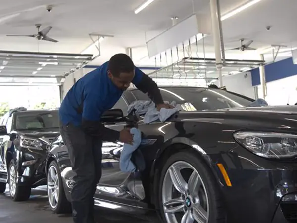 A MEGA Auto Spa detailer hand-drying a black BMW inside the detail center