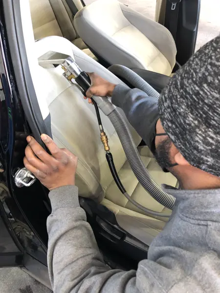 A MEGA Auto Spa detailer vacuuming the seat of a car with a crevice tool