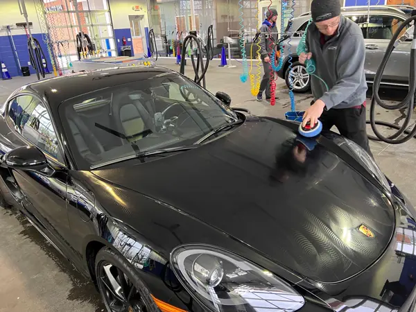 A detailer machine-polishing the hood of a black sports car