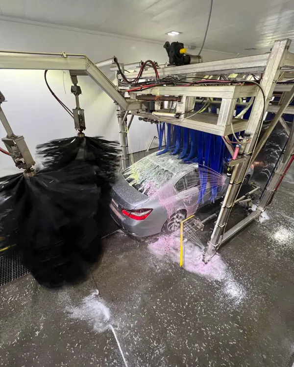 A car in the MEGA Auto Spa tunnel, covered in pink foam between the wash brushes